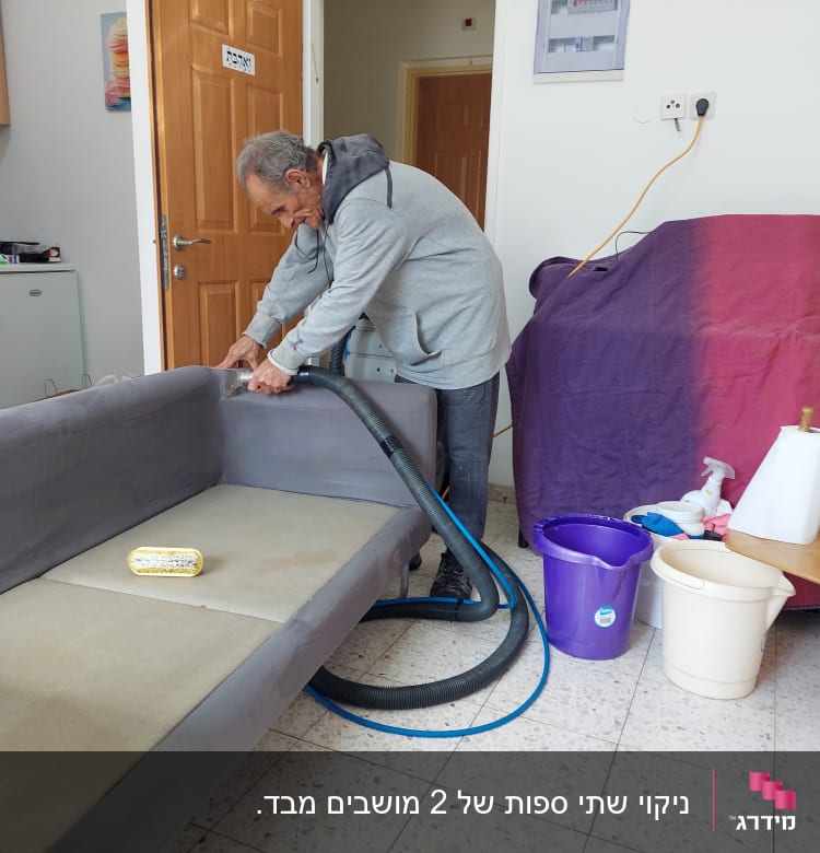 אדם מנקה ספה עם שואב אבק, דלי וסבון